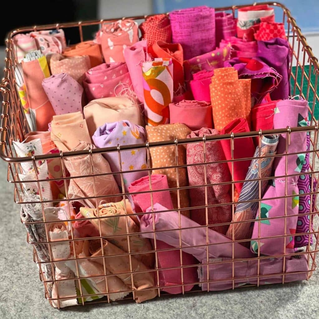 A view of pink fabrics rolled up and stored inisde a wire basket