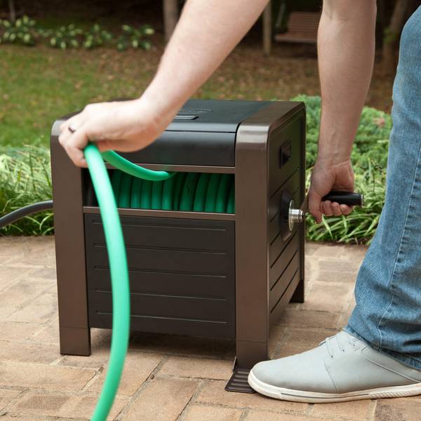 a person pulling green pipe from garden hose reel in brown color