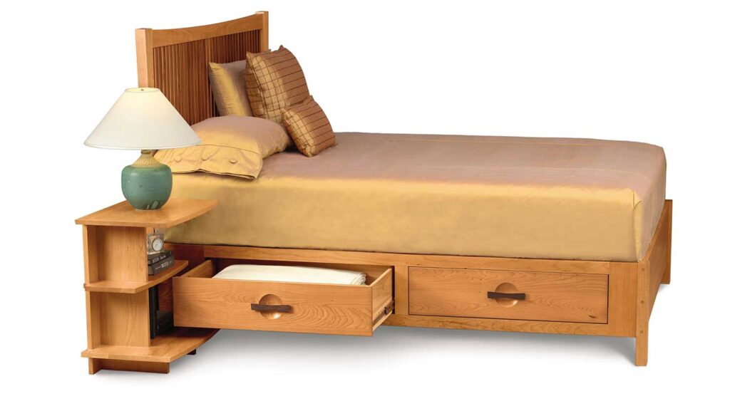 A view of a wooden bed with drawer opened under it by a bed side table