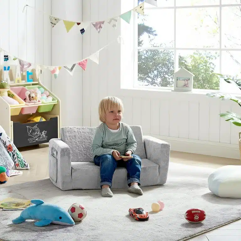 a kid sitting on a convertible small sofa toys scattered around