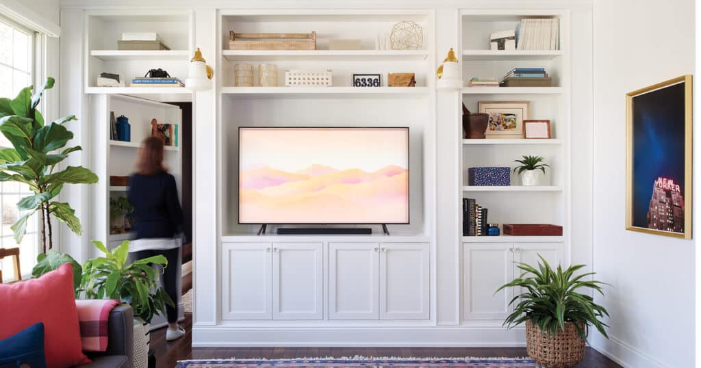 a woman entering through the door of hidden bookshelf an LED placed different decor items organized in the shelves