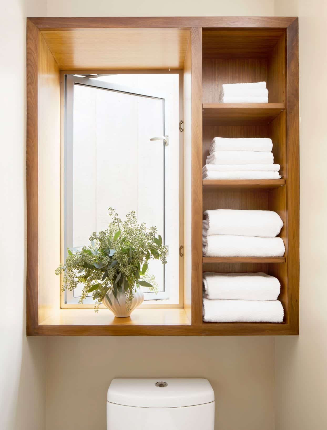 A view of towels stored over a toilet inside a wooden shelf