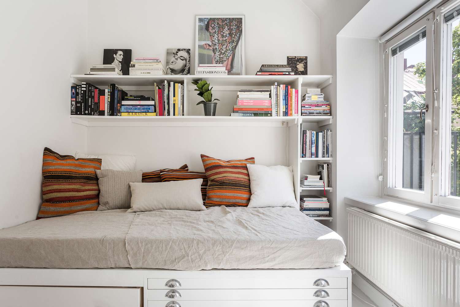 A front view of a bedroom with a shelf for book storage over the bed