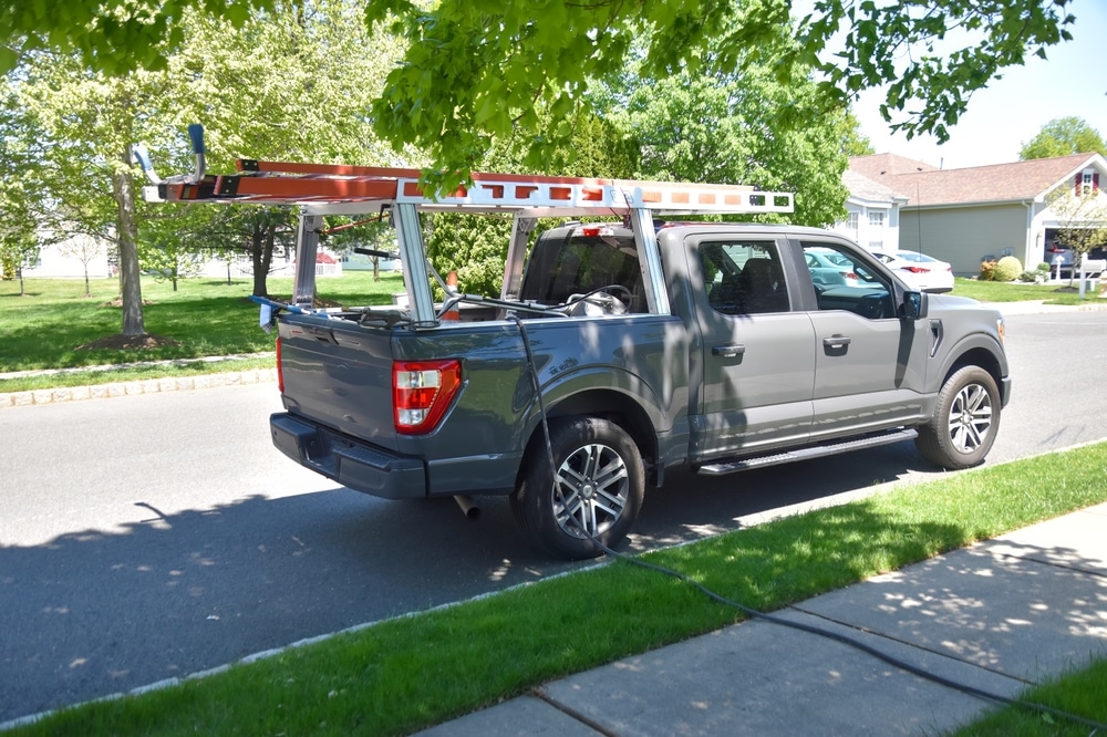 A side view of a grey truck with ladders stored inside the racks of the bed